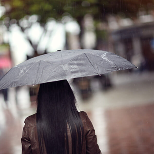 Rain drops falling on a woman holding a black umbrella in a shopping street scene concept for bad weather, winter or protection